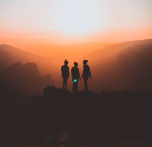 three silhouettes of women's figures against a sunset over mountains