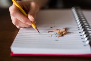 hand holding a yellow pencil and writing in a notebook