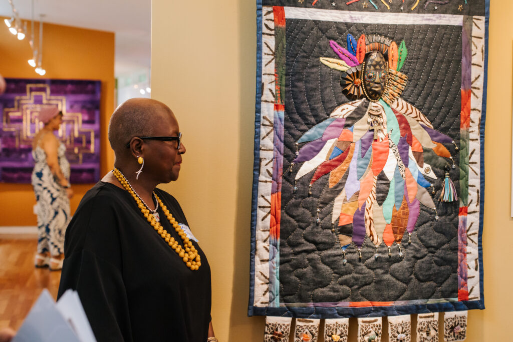A woman stands in front of her quilt