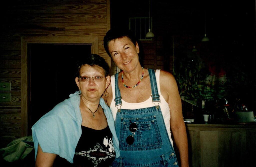 Two women, one in overalls, smile at the camera