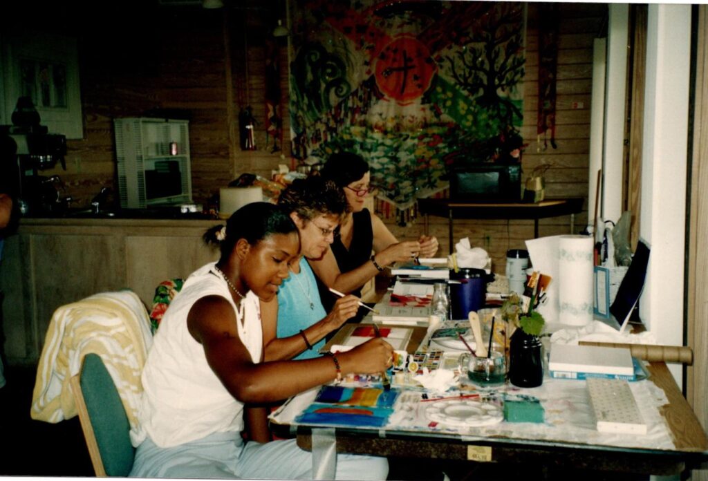 A group of women sit at a long table working on paintings