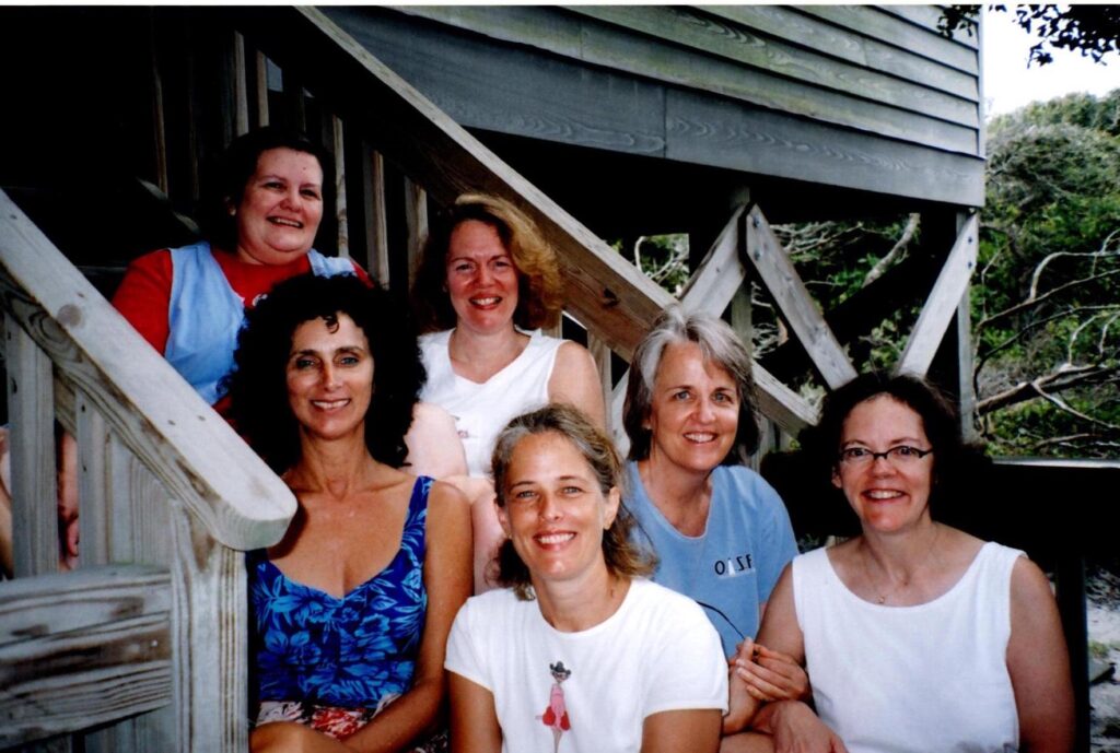 A group of six women sit on steps at the beach
