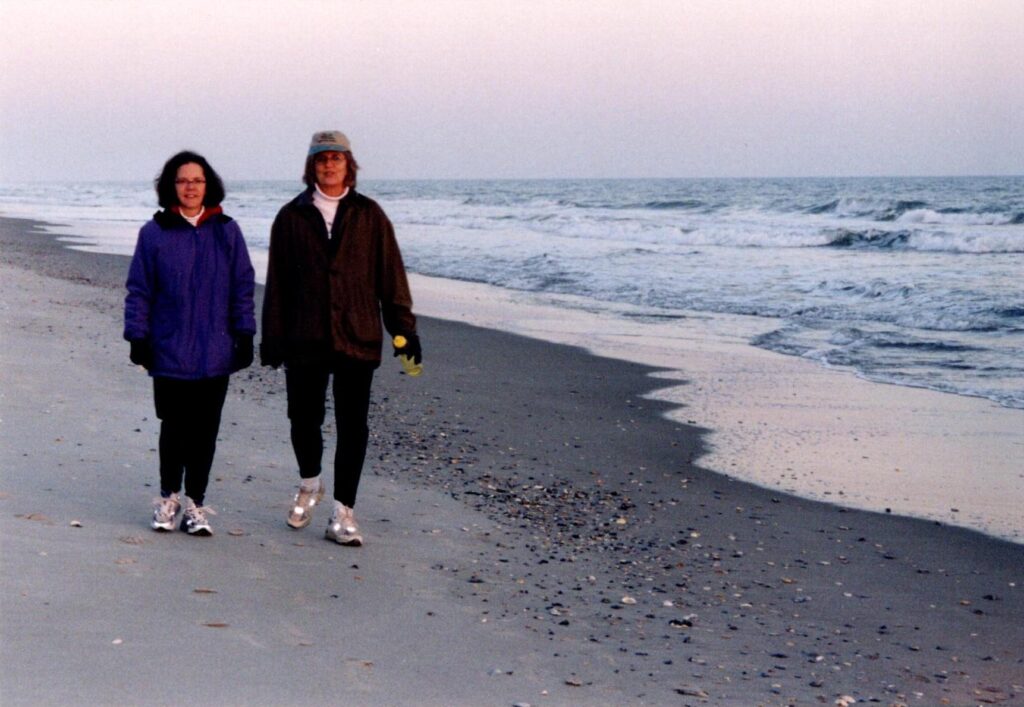 Two women walk along the beach at dusk
